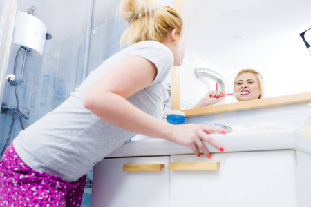 女人刷清洁牙齿特写。有趣的金发女郎，用牙刷在浴室里。口腔卫生。不寻常的广角视图