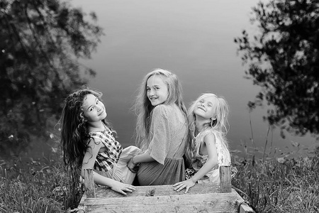 三可爱的小女孩在河岸上。暑假。愉快的女朋友在度假, 姐妹在河上, 友谊, 幸福和家庭