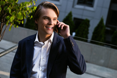 商务电话。一个英俊的年轻人站在户外, 微笑着说着手机