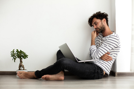 年轻人坐在地上,手提电脑和一棵植物照片