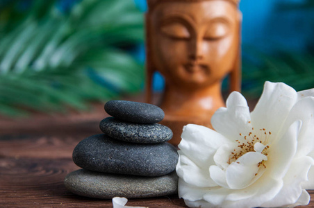 金字塔的灰色禅宗石头与美丽的新鲜白色的花朵绿叶和佛像在木质背景.