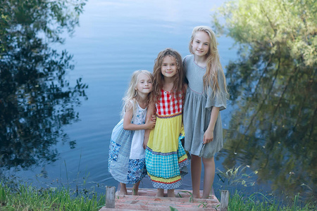 三可爱的小女孩在河岸上。暑假。愉快的女朋友在度假, 姐妹在河上, 友谊, 幸福和家庭