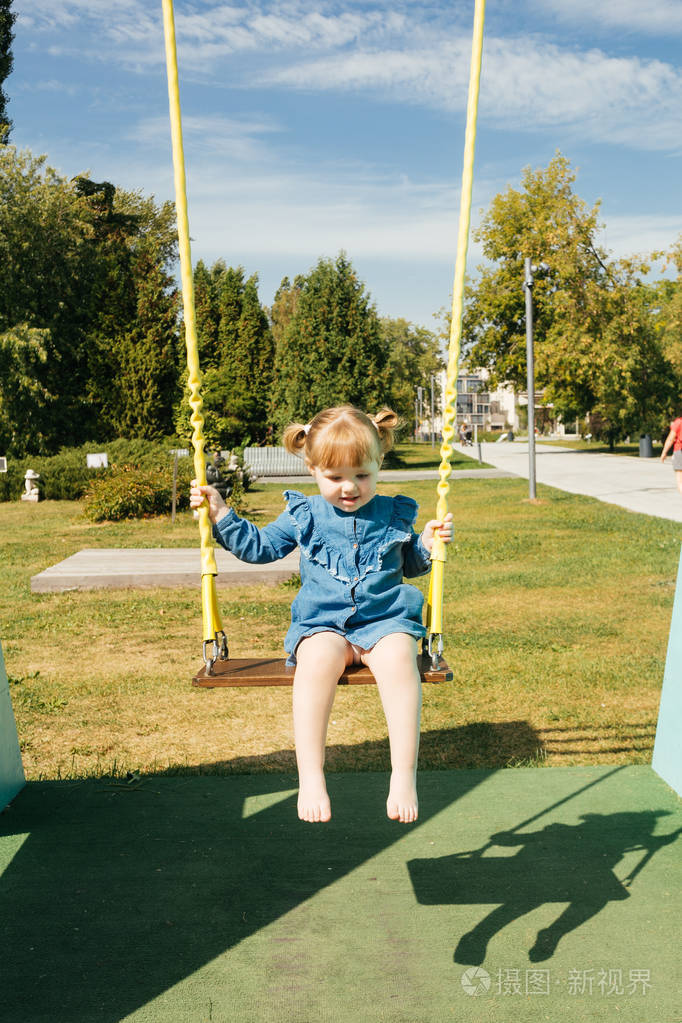 一个3岁女孩的肖像在操场上的秋千上一个城市公园在一个温暖的阳光
