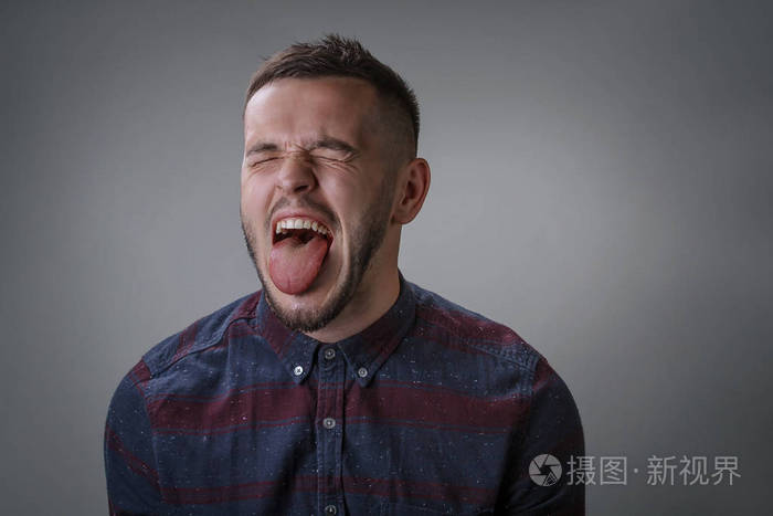 成年男子在一个格子衬衫与胡须宽张开嘴上的刚毛伸出舌头和闭上眼睛