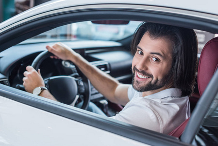 坐在新车上的微笑胡子男子在经销商沙龙测试驱动器