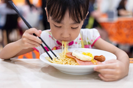 亚洲华人小女孩在餐厅用筷子吃面条