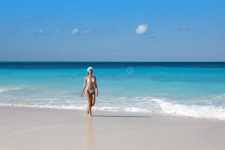 穿着白色性感比基尼的女人在碧绿的海洋中漫步在一个令人讨厌的海滩上