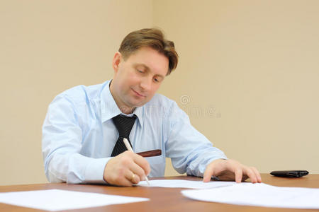 打领带的商人坐在桌旁签署文件