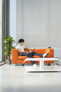 办公室橙色沙发上使用笔记本电脑的男子