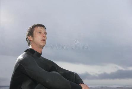 体贴的男冲浪者坐在沙滩上阴云密布的天空中