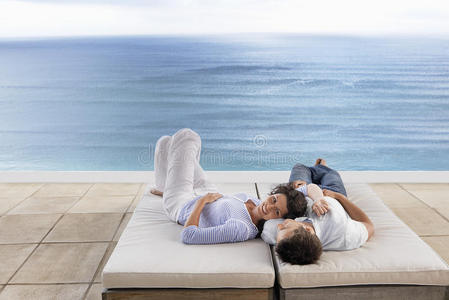 一对浪漫的夫妇在无限游泳池旁的日光浴床上放松