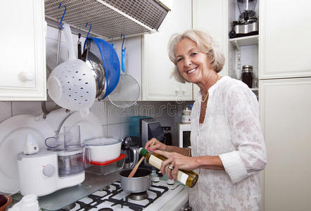 厨房柜台的老太太往平底锅里加橄榄油的画像