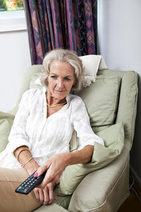 家中扶手椅上带遥控器的老年妇女换频道
