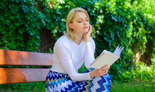 女金发女郎在公园看书时休息放松.女孩坐板凳放松与书, 绿色自然背景.