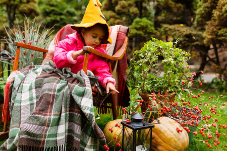 可爱的小女孩穿着万圣节服装坐在装饰秋天花园扶手椅的乐趣