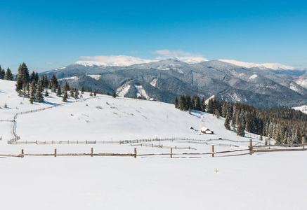 风景如画的雪冬山坡和孤独的农舍在高原农庄, 在乌克兰。Chornohora 山脊全景和 Pip 的伊万山与天文台顶部在云层后面