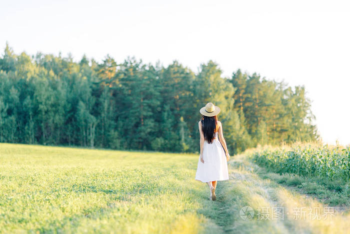 女孩走在田野上, 在帽子和夏季礼服.
