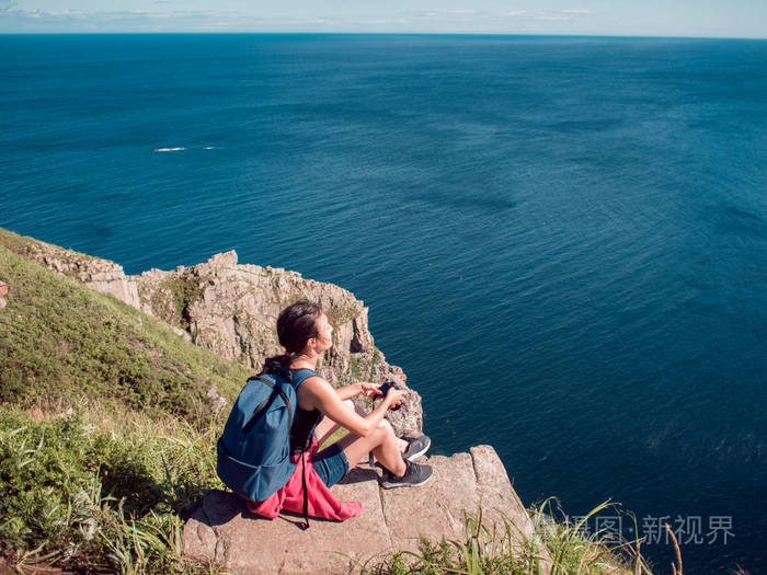 年轻女子摄影师坐在悬崖边上, 风景.美丽的岩石海岸