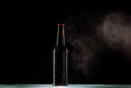 带喷水的啤酒瓶在黑色背景表面周围照片