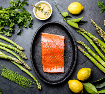 生鲑鱼鱼片。芦笋, 柠檬, 橄榄油和香草在盘子里与鲑鱼。食品烹饪背景。顶部视图
