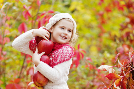 美丽的小女孩在秋季花园里捧着苹果。.小女孩在苹果树果园玩。孩子在秋季收割时吃水果。儿童户外娱乐。健康营养
