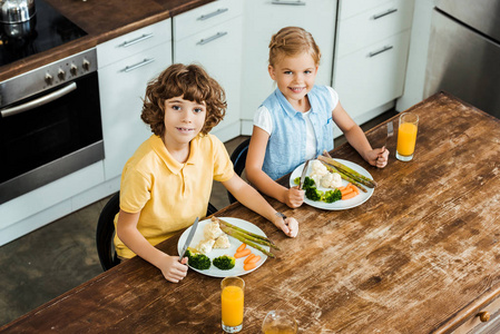 高角度看可爱快乐的孩子吃健康的蔬菜和微笑的相机
