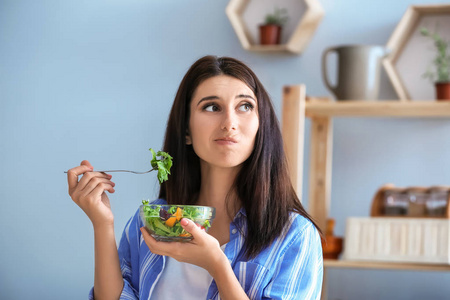 不情愿的女人吃健康的沙拉和蔬菜在室内。饮食理念