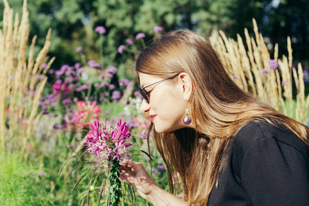 在一个温暖的阳光明媚的日子, 一个女人的肖像在城市公园里闻到一朵花的香味。