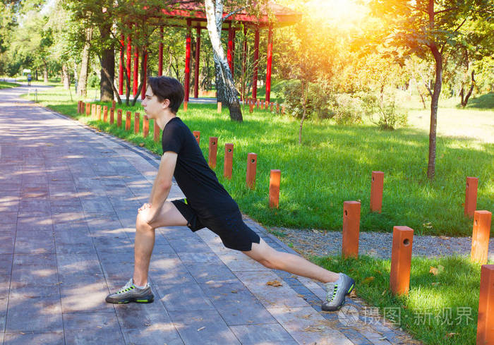 照片 年轻的健身男子在公园锻炼.男人做伸展运动 准备晨练 跑步.