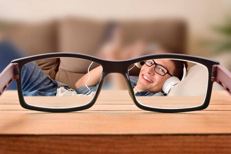聚焦场景视觉矫正的概念观通过戴眼镜的年轻人的眼镜娱乐躺在沙发上