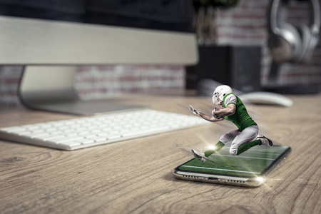 足球运动员与一个绿色制服播放和从一个完整的屏幕电话在一个木桌上。观看足球比赛的需求概念。复制空间