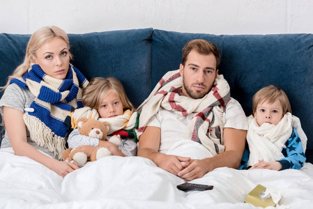 生病的年轻家庭在围巾看着相机, 而躺在床上