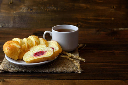 自制的蛋糕奶油奶酪和草莓果酱和白色杯茶在黑暗的木质背景的糕点