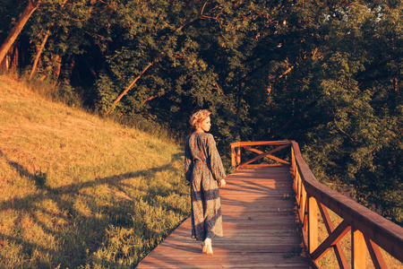 女人在一个温暖的夏日漫步在公园里, 看着夕阳