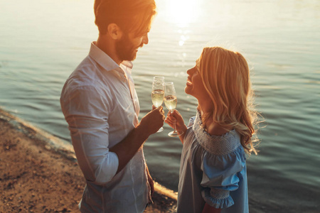 愉快的年轻夫妇在河边的户外葡萄酒举杯