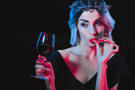 拿酒杯吸血鬼妇女拿着酒杯的血, 舔她的手指被孤立的黑色照片