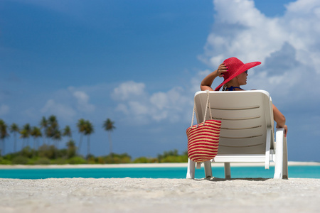 年轻女子在躺椅在热带海滩上晒日光浴