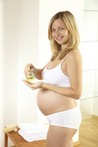 金发孕妇穿着白色内衣浇注身体油按摩她的肚子在浴室