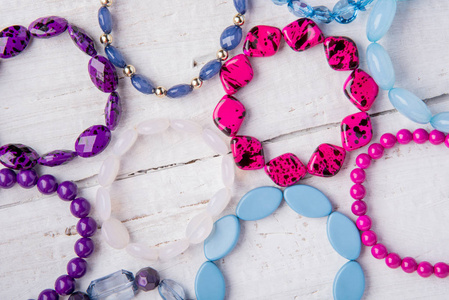 在白色木质背景上的几个美丽的珠子和蓝色, 粉红色和紫色的宝石手镯