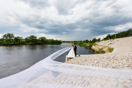 新郎和新娘很长的婚纱站在河岸边