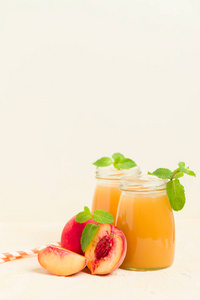 桃冰沙在玻璃罐子与新鲜成熟的果子和绿色薄荷叶子在黄色柔和的背景原始的甜甜点或早餐饮料为健康有机饮食概念
