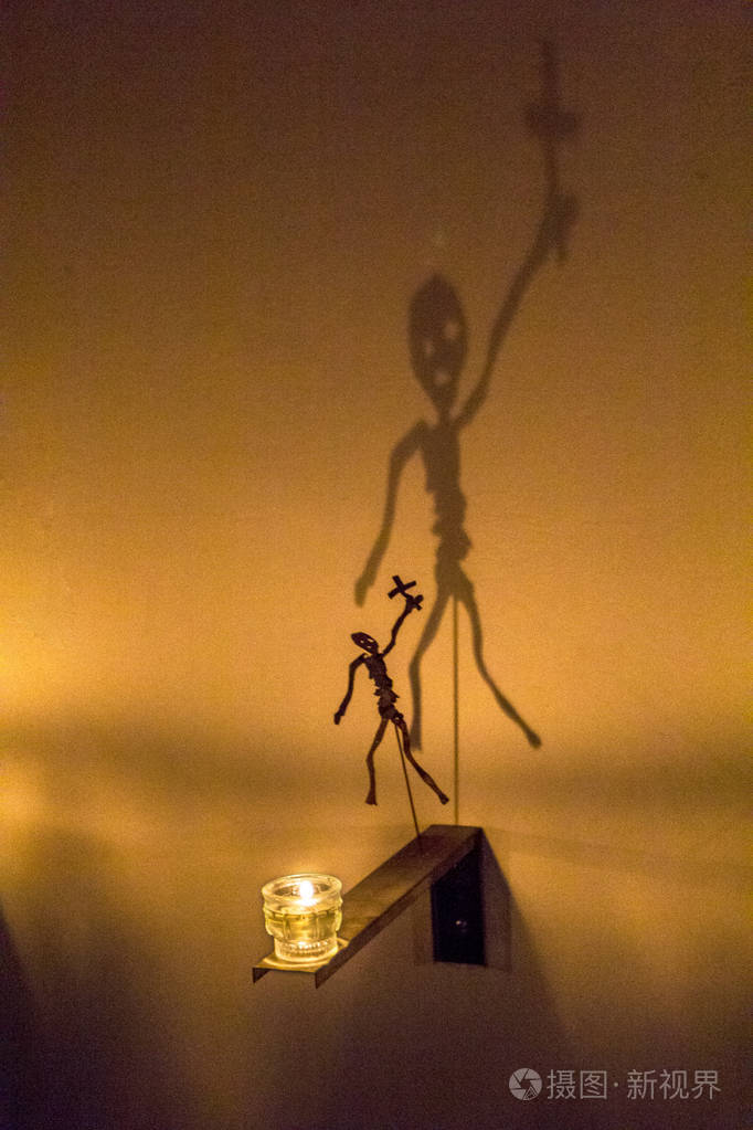 有十字架的骷髅的神话般的影子从蜡烛的火焰上反射到墙上.