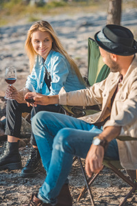 愉快的年轻夫妇与喝红酒的杯子在野餐期间谈话
