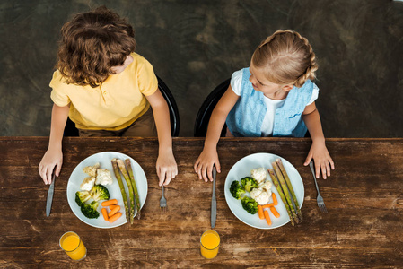 高角度看可爱的孩子吃健康的蔬菜和看着对方