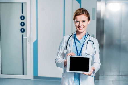 微笑的女医生与听诊器在颈部显示数字平板电脑空白屏幕在医院