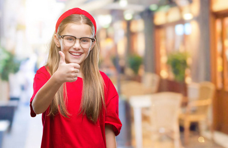 年轻漂亮的女孩戴着眼镜在孤立的背景下做快乐大拇指手势与手。批准表达式看相机与显示成功