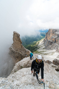 一群年轻的登山者在陡峭的通过 Ferrata 与意大利白云岩的宏伟的看法在他们后面巴迪亚