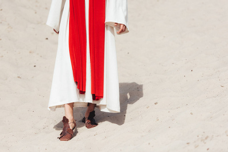 被裁剪的耶稣在长袍, 红色窗扇和凉鞋漫步在沙漠中的沙子的形象