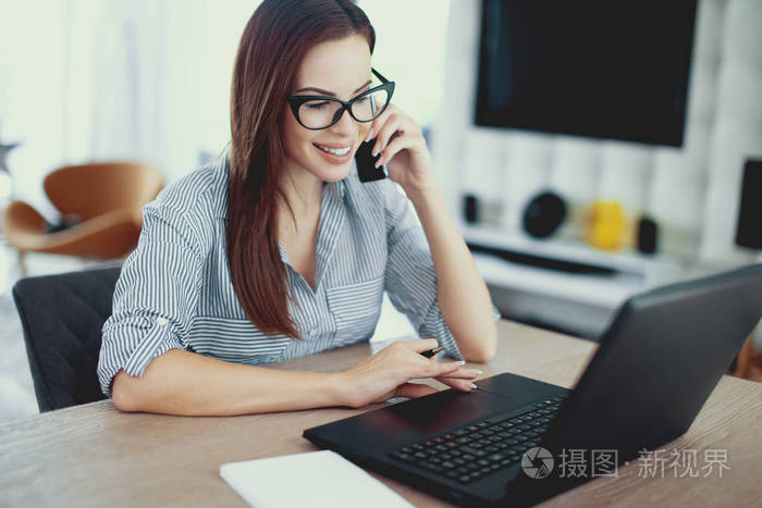 书自由职业者的女人打电话与微笑在笔记本电脑室内