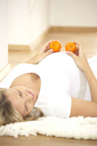 愉快的怀孕妇女与橘子躺在地毯在家里